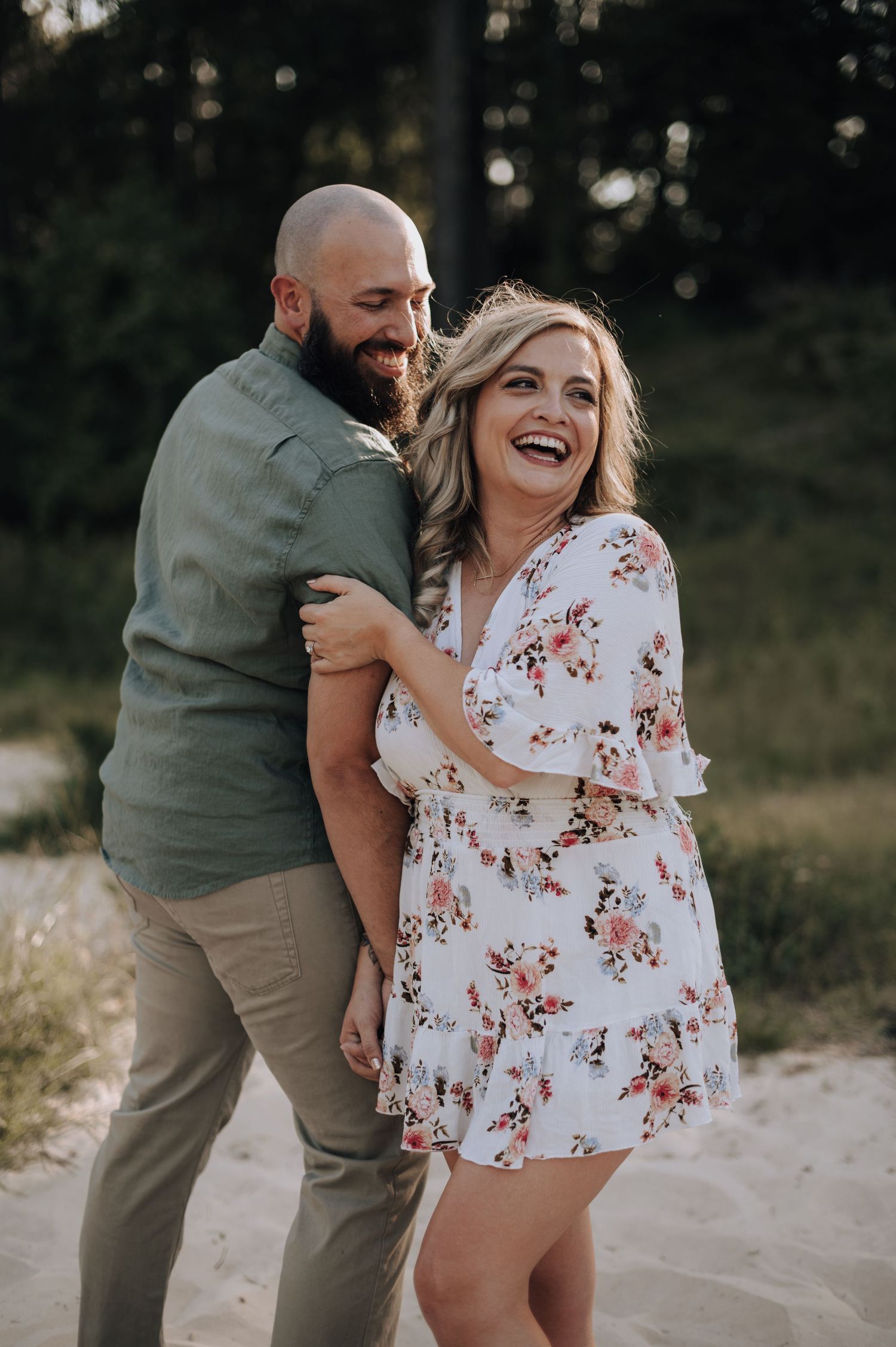 Candid engagement photo of couple laughing together outdoors at sunset.