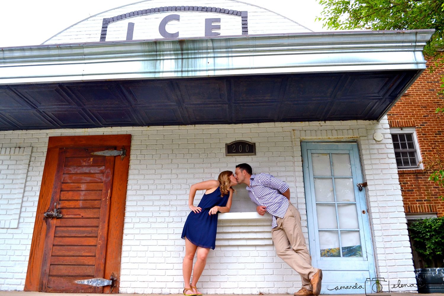 Romantic couple posing playfully against a white brick building with 'ICE' signage.