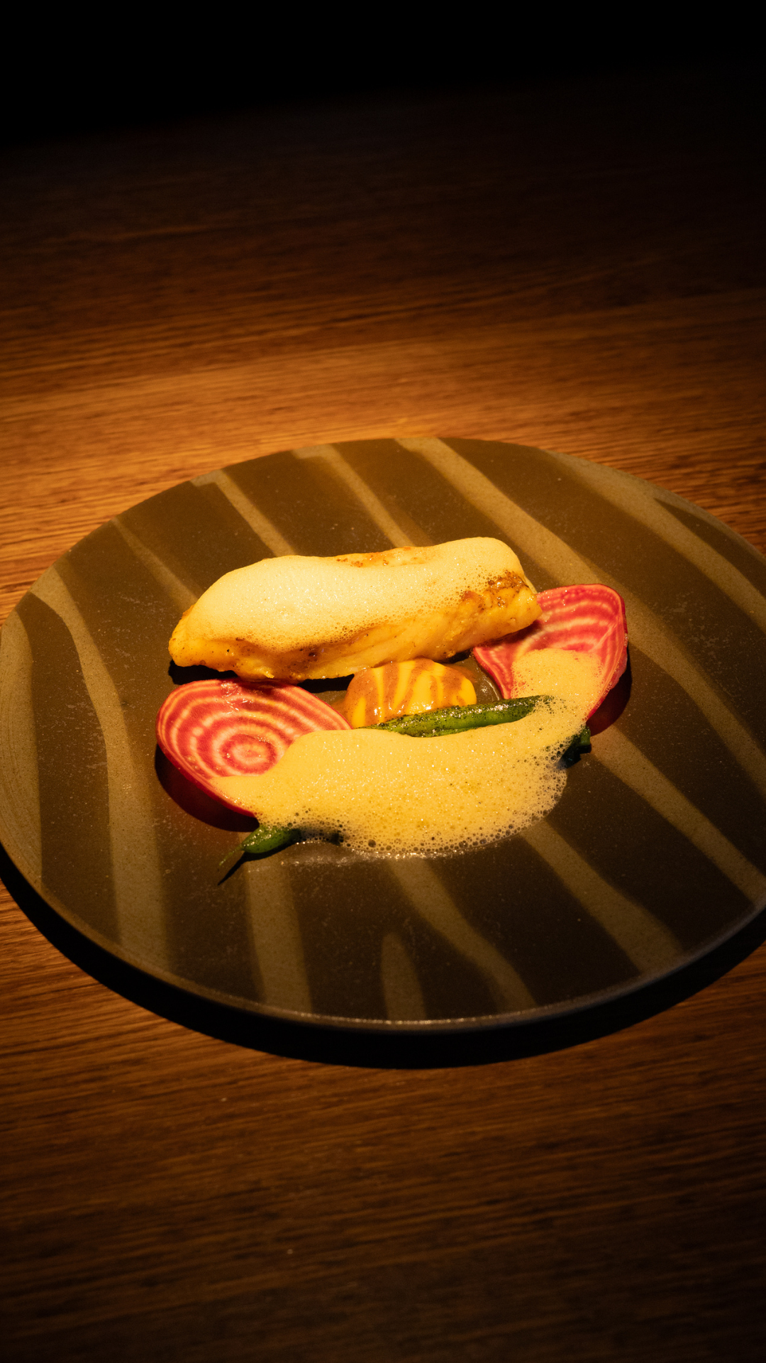 Artisanal sandwich on dark plate with striped pattern and sliced red and white radishes.