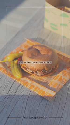 A gourmet burger with pickles served on an orange patterned paper.