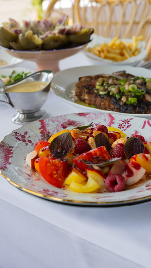 A vibrant plate featuring sliced tomatoes, citrus, and berries alongside grilled meat and french fries.