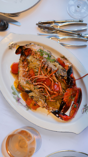 Whole lobster dish with sauce and vegetables served on white platter with wine glass.