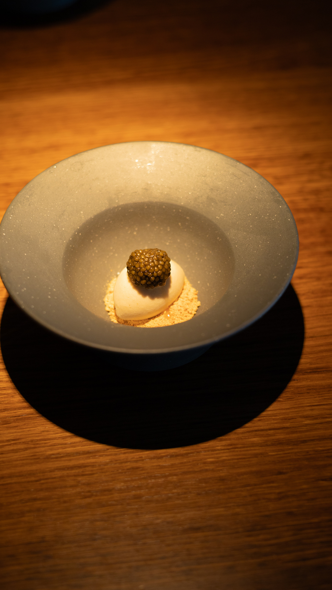 Artfully plated dessert featuring caviar and ice cream in a minimalist gray bowl with dramatic lighting.