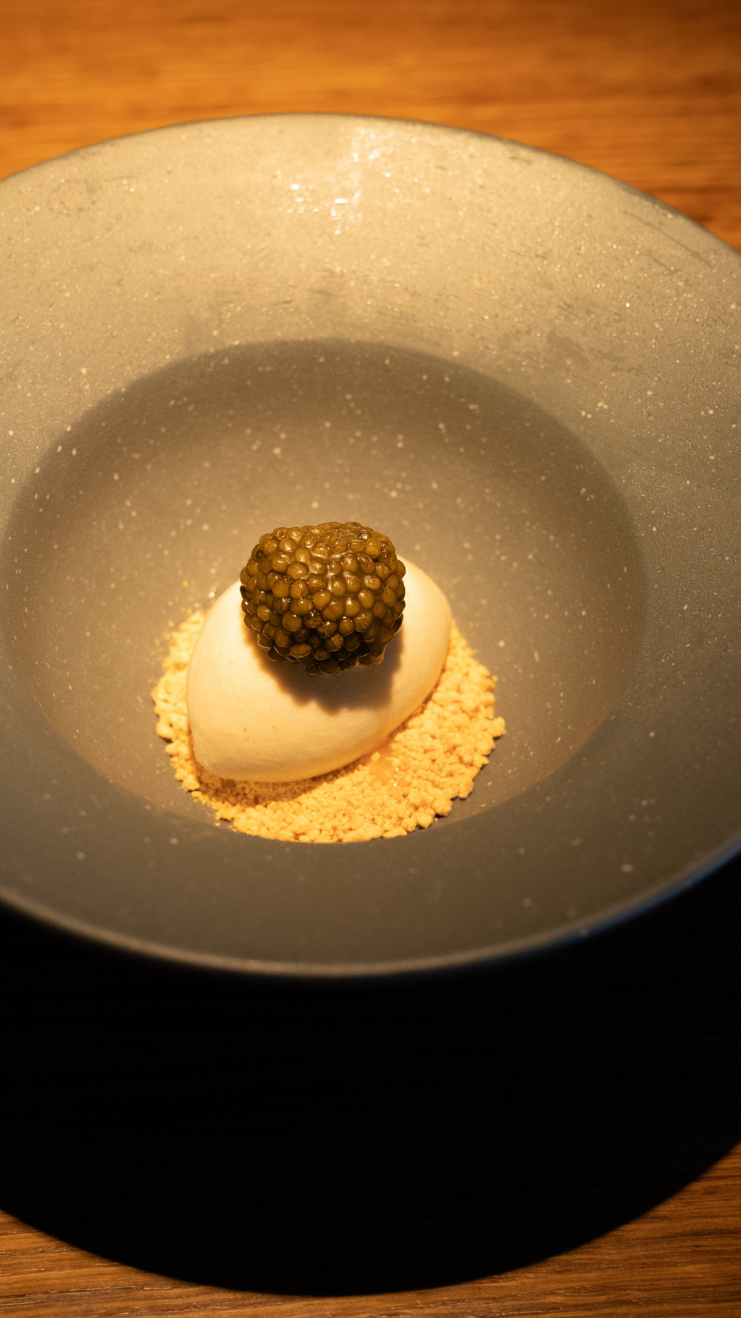 Spherical black caviar atop cream-colored ice cream on a powder bed in a modern gray bowl.