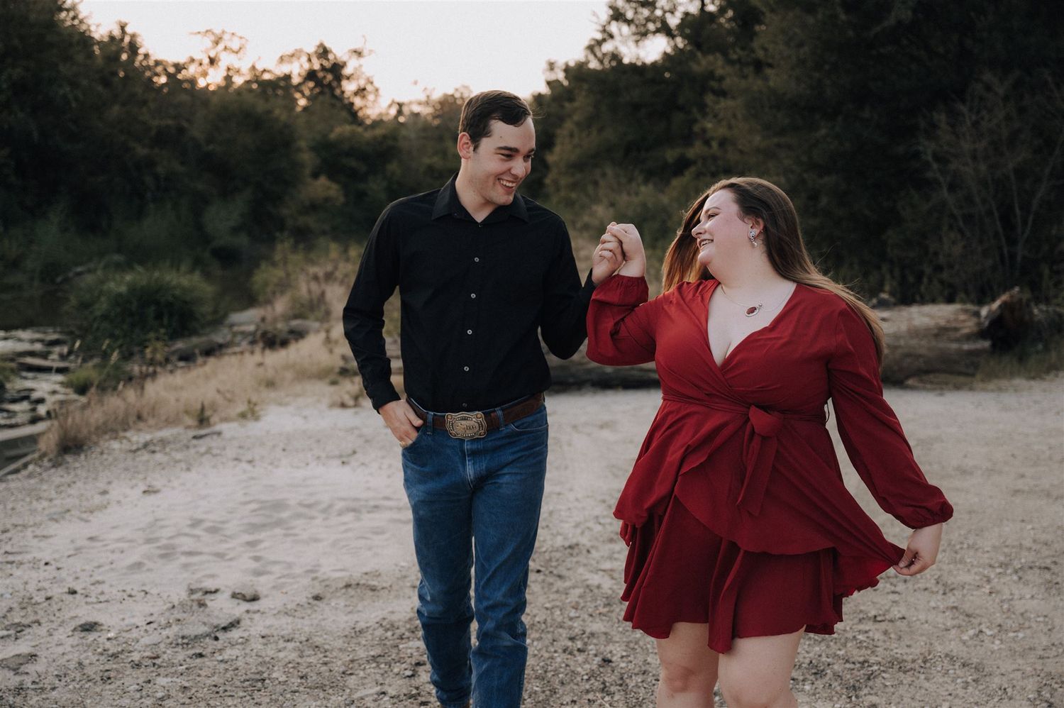 Couple laughs together while walking along a scenic outdoor trail at sunset.