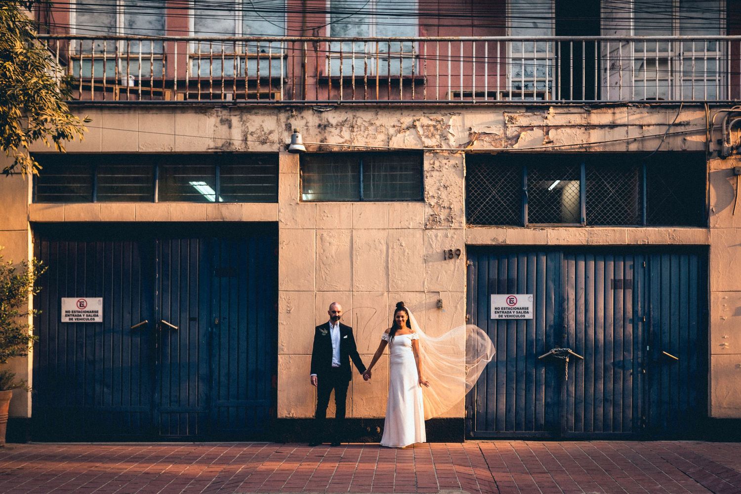A wedding couple poses against industrial garage doors in an urban setting.