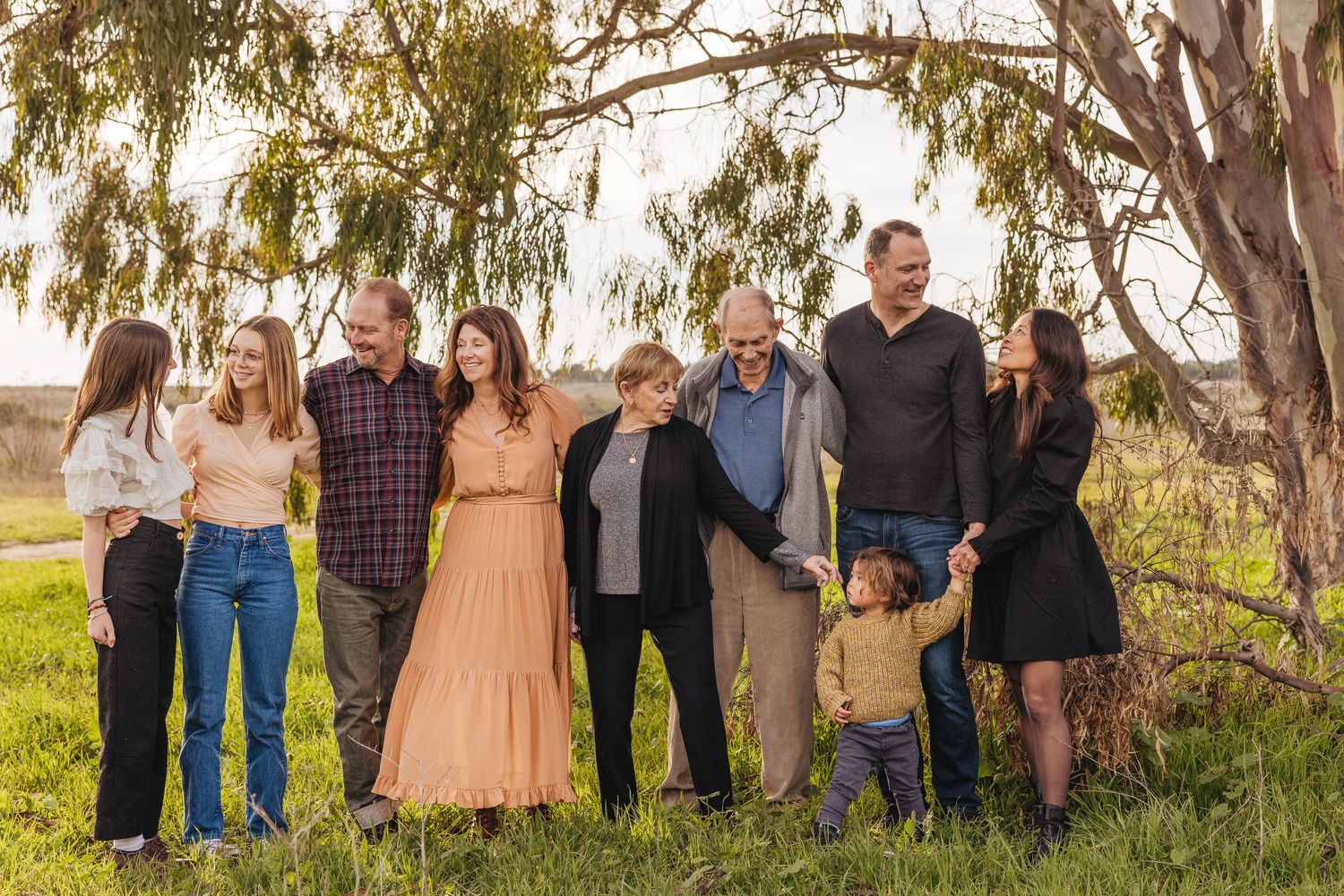 A multigenerational family gathering under eucalyptus trees in casual attire.