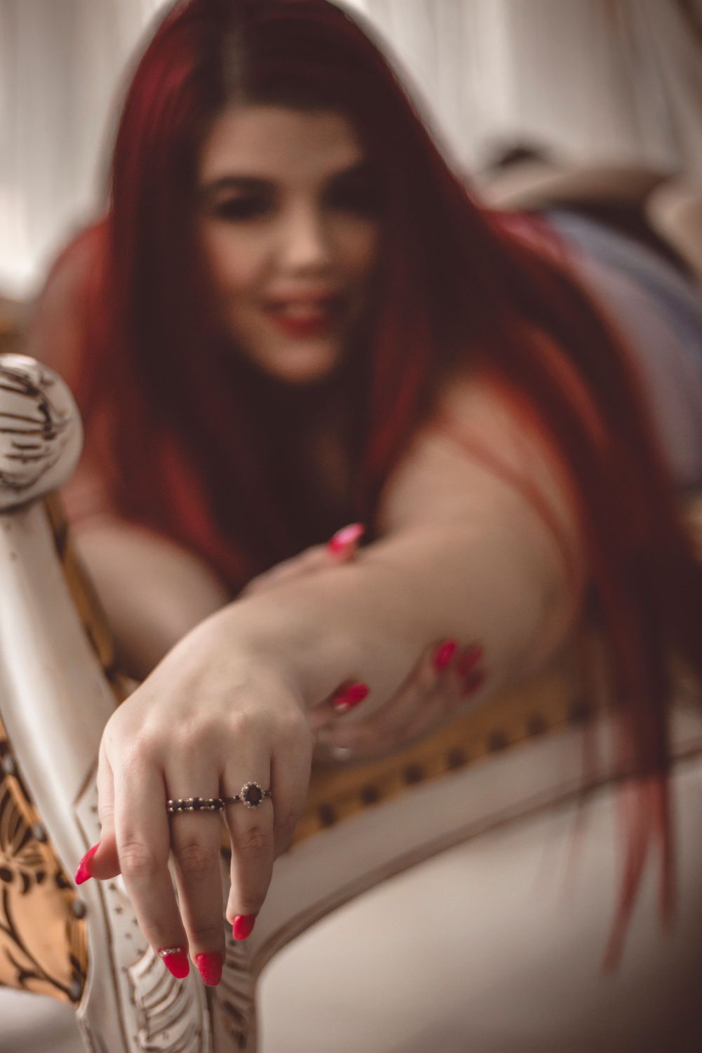 Intimate portrait with red hair and nails reaching toward camera with soft romantic lighting.