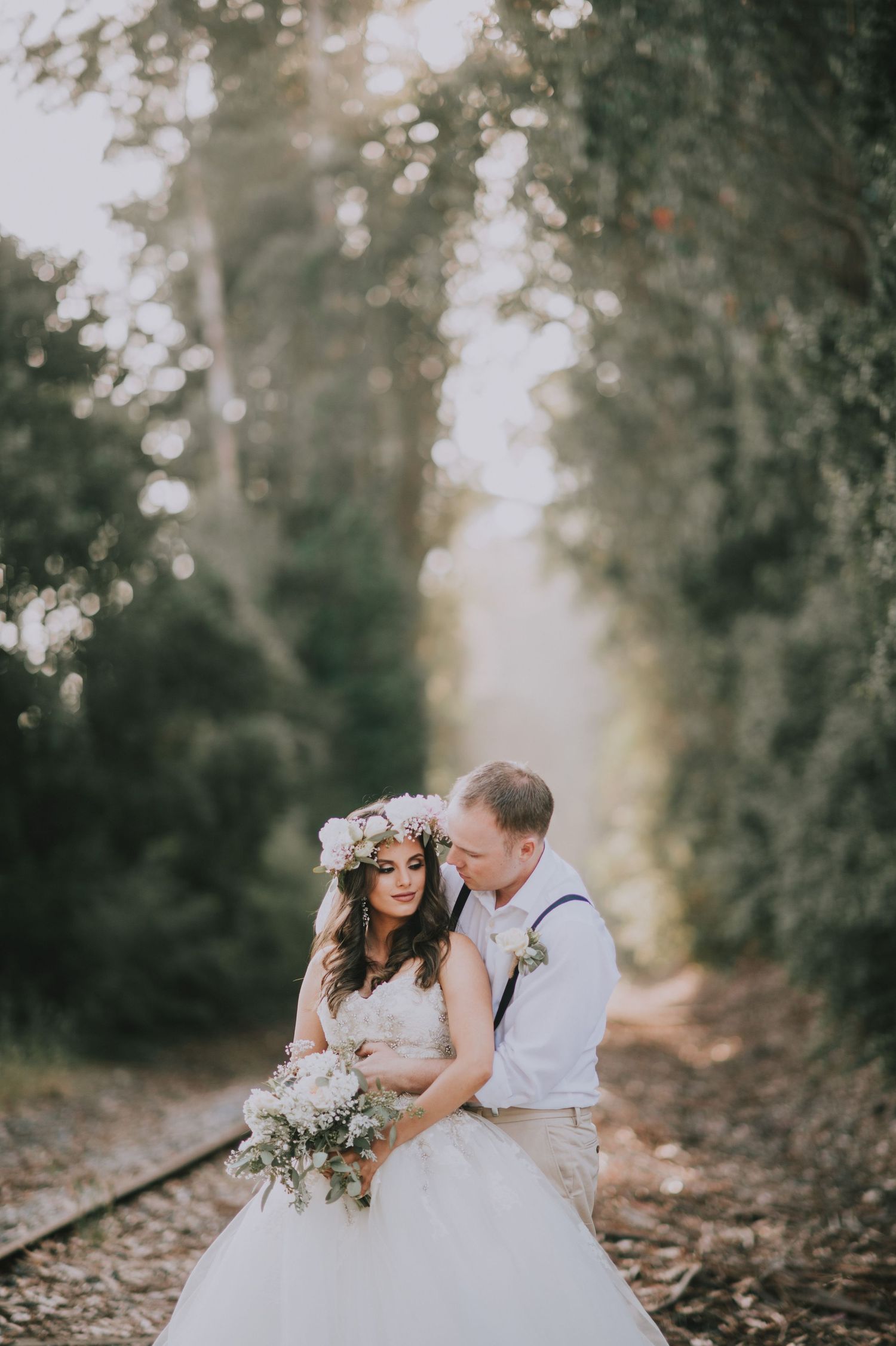 A couple poses on rustic train tracks surrounded by dreamy forest scenery.
