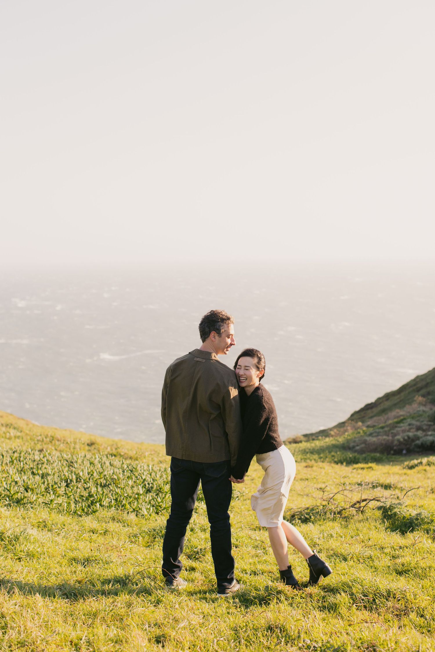 Sweet moment shared between couple on a green hillside overlooking the sea.