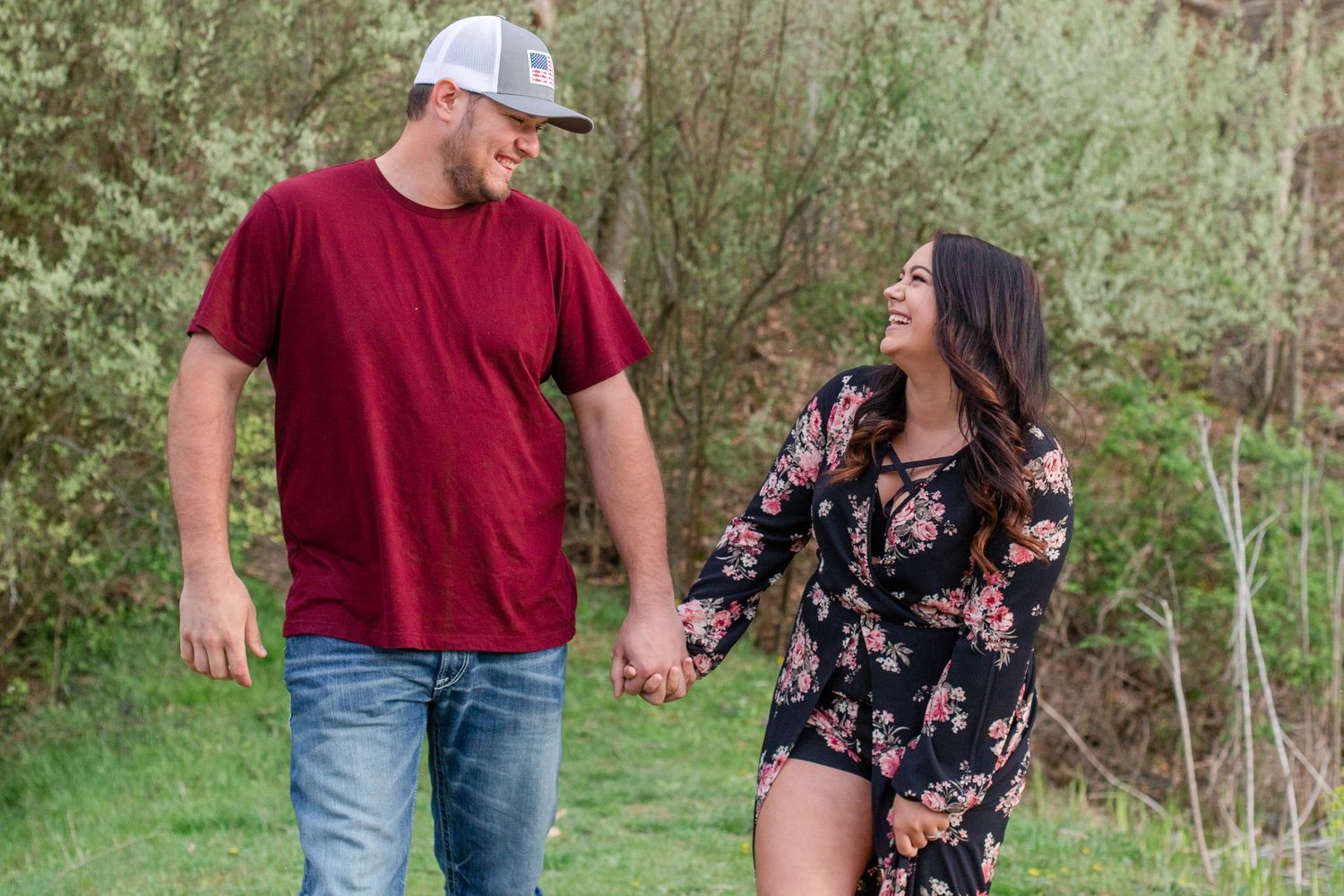 Couple holding hands while walking outdoors, wearing red shirt and floral dress.