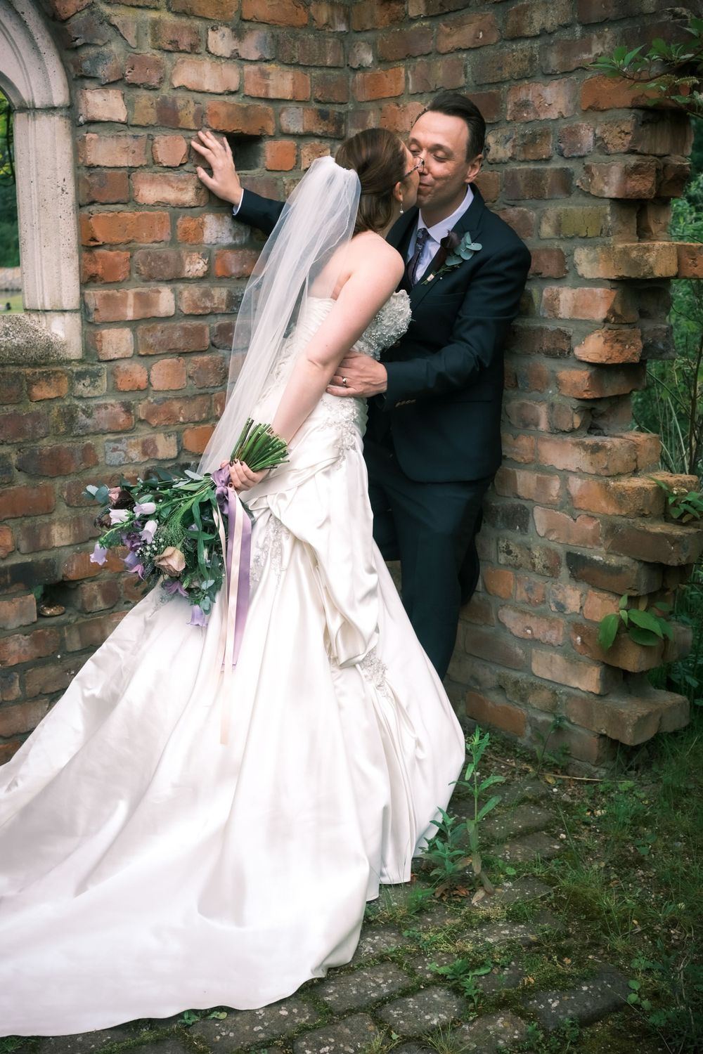Romantic wedding portrait against brick wall with flowing white dress and floral bouquet.