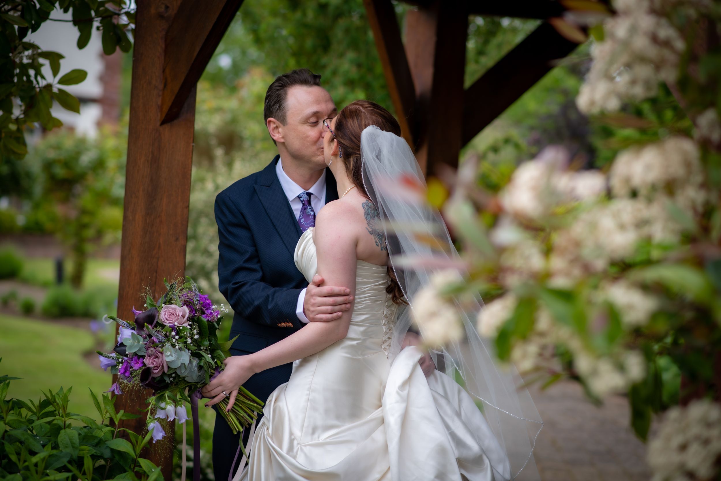 Intimate wedding moment under wooden gazebo surrounded by spring flowers.