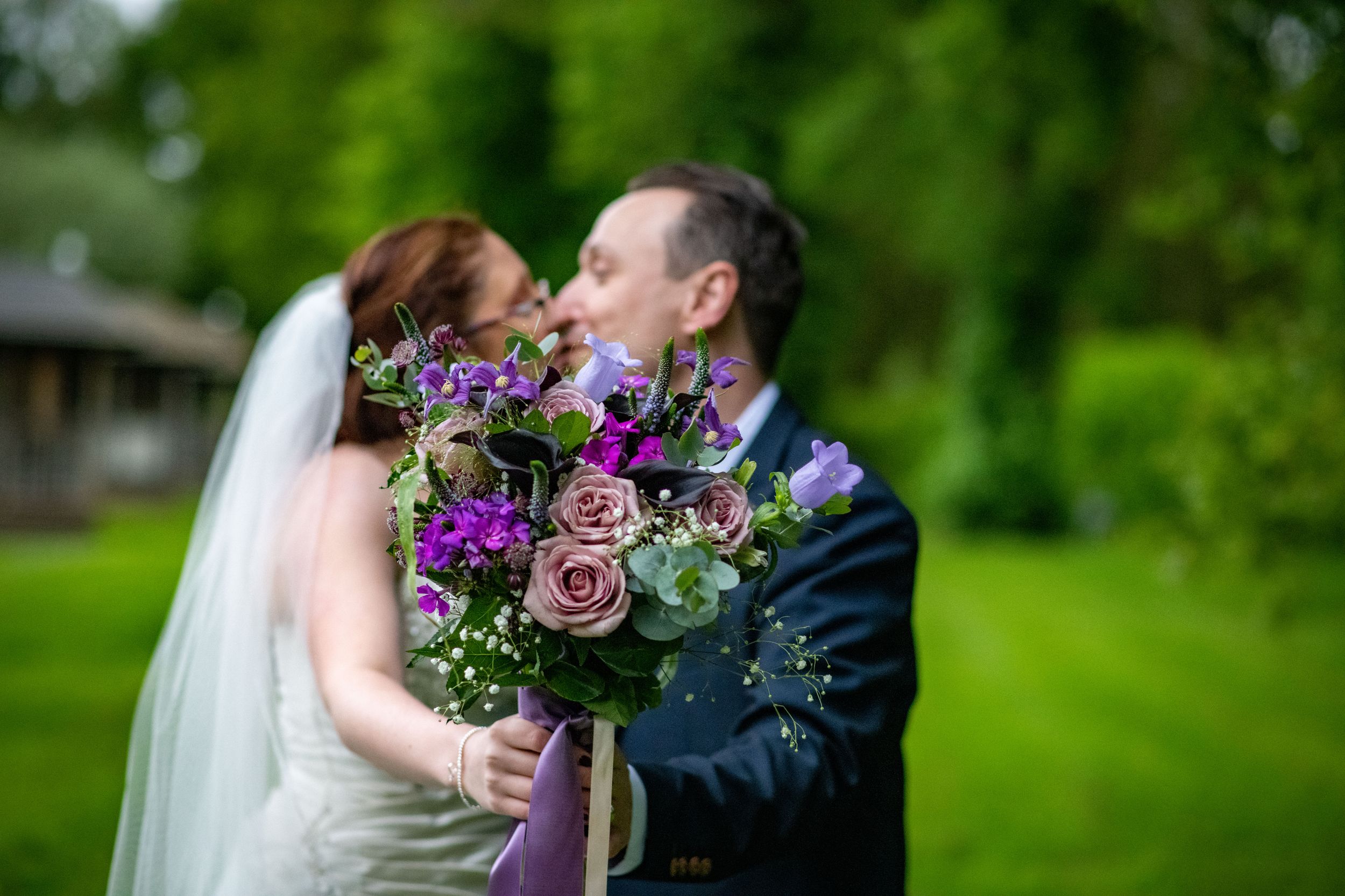 Romantic wedding portrait with purple floral bouquet in garden setting.