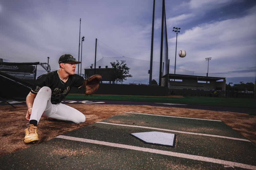 Baseball player catching at home plate on dirt infield during evening practice.