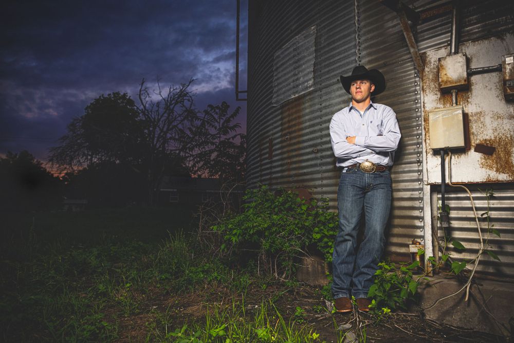 Person in western attire standing against metal building at dusk.