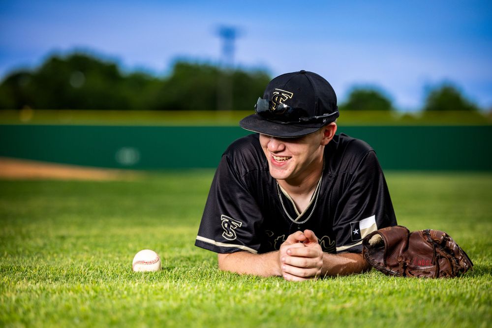Baseball player lying on grass field with baseball and glove during sunny day.