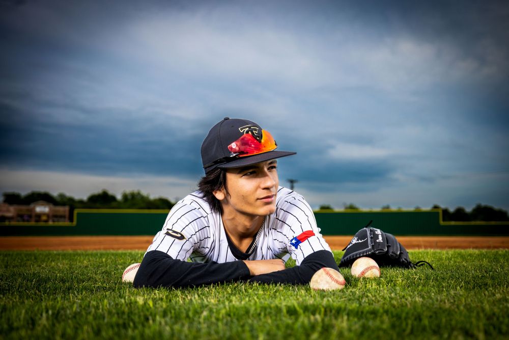 Baseball player in uniform lying on grass field with baseball beside them under moody sky.