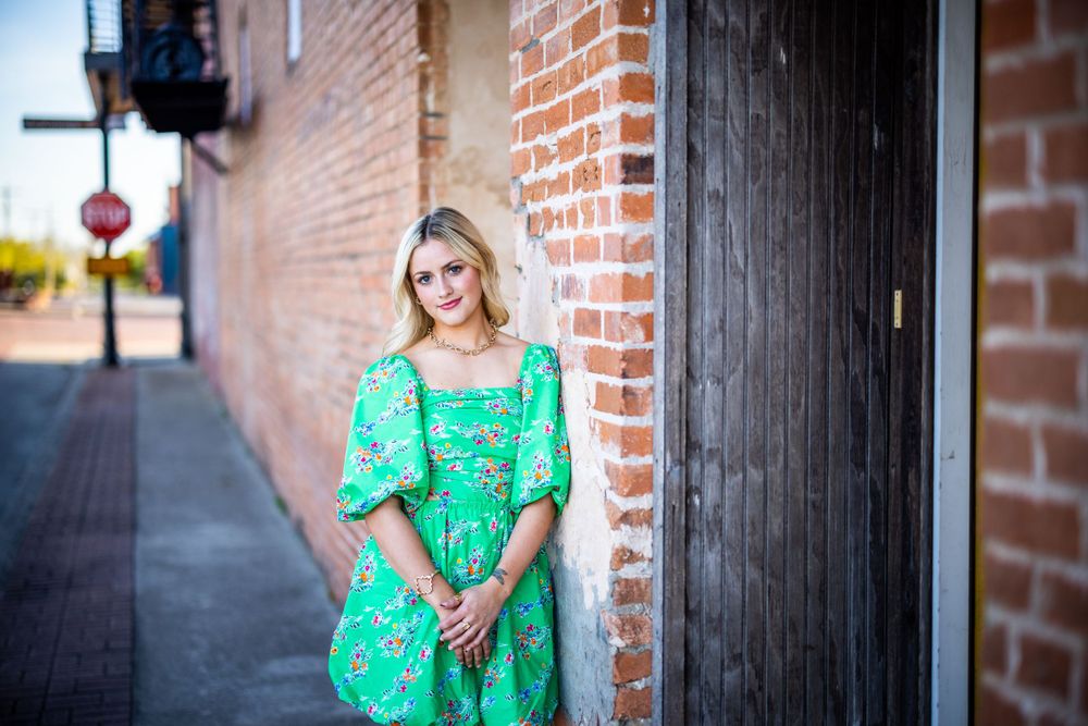 Street style portrait in green floral dress against brick wall downtown.