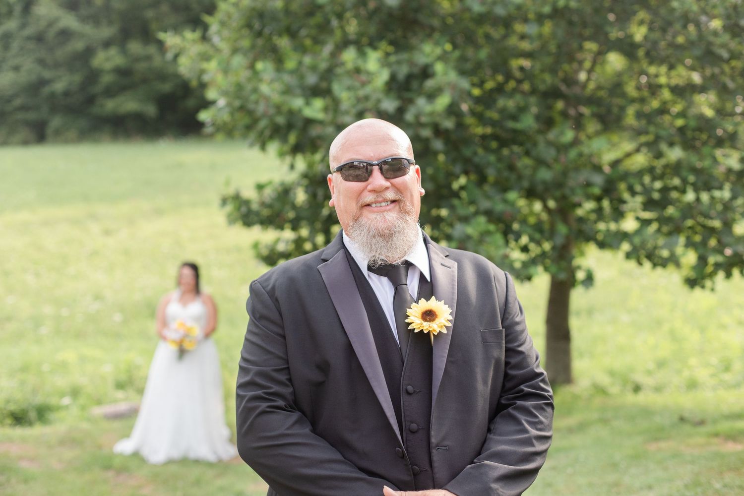 Wedding party members in formal attire pose casually on a grassy hillside for outdoor portraits.