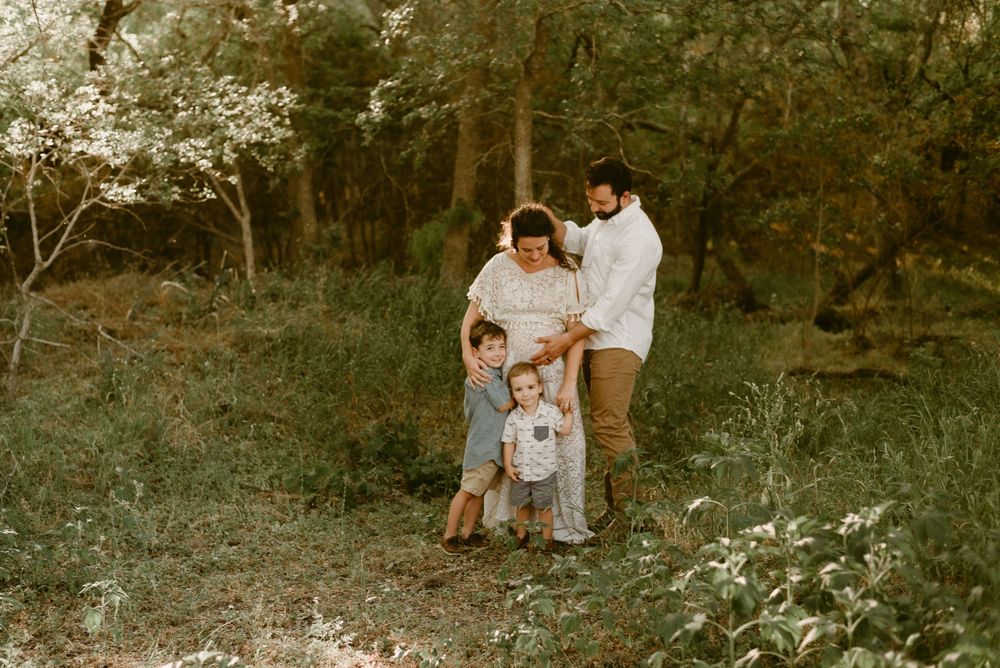 Family embracing in a sunlit forest clearing.