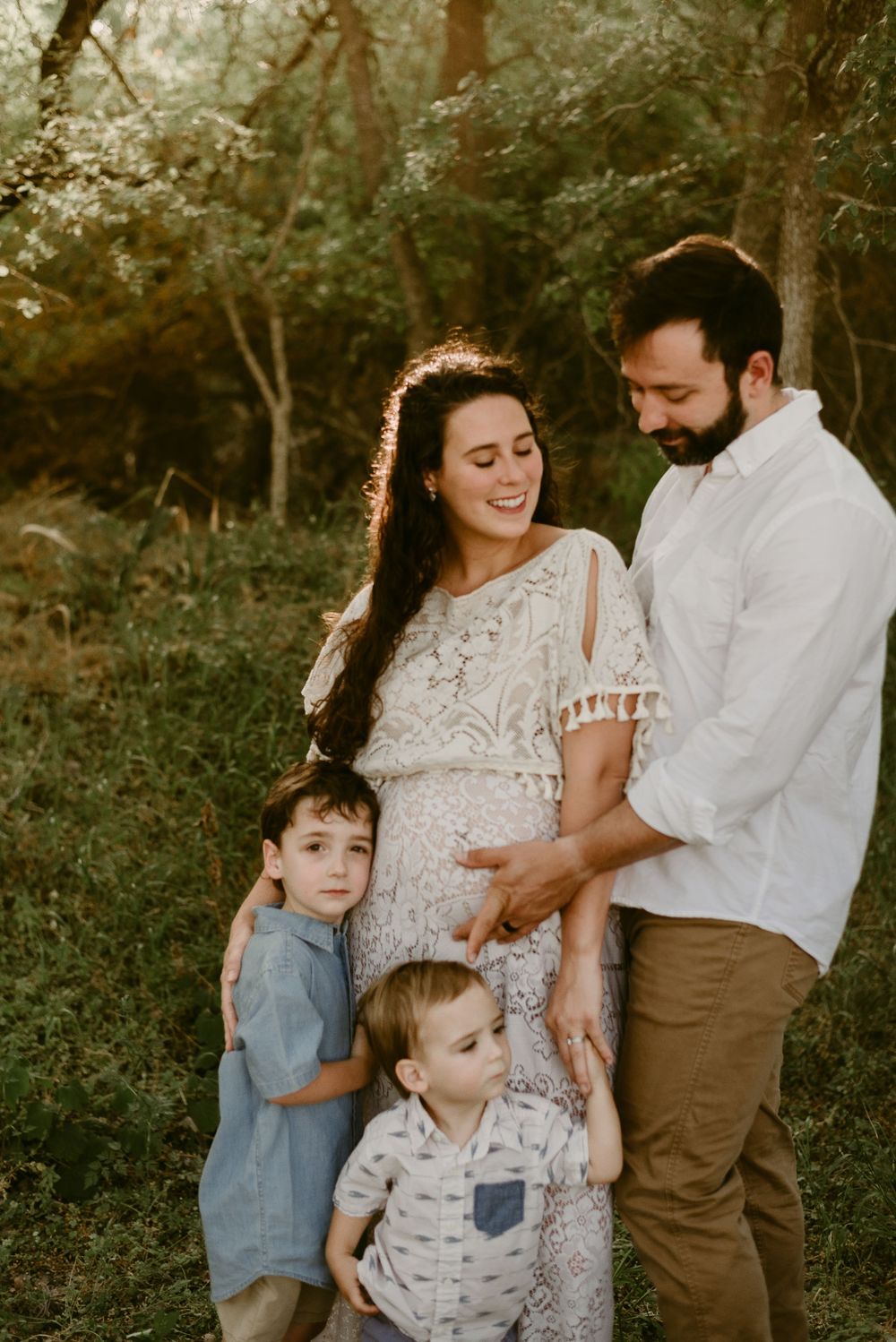 Family of four poses together in a woodsy setting during sunset.