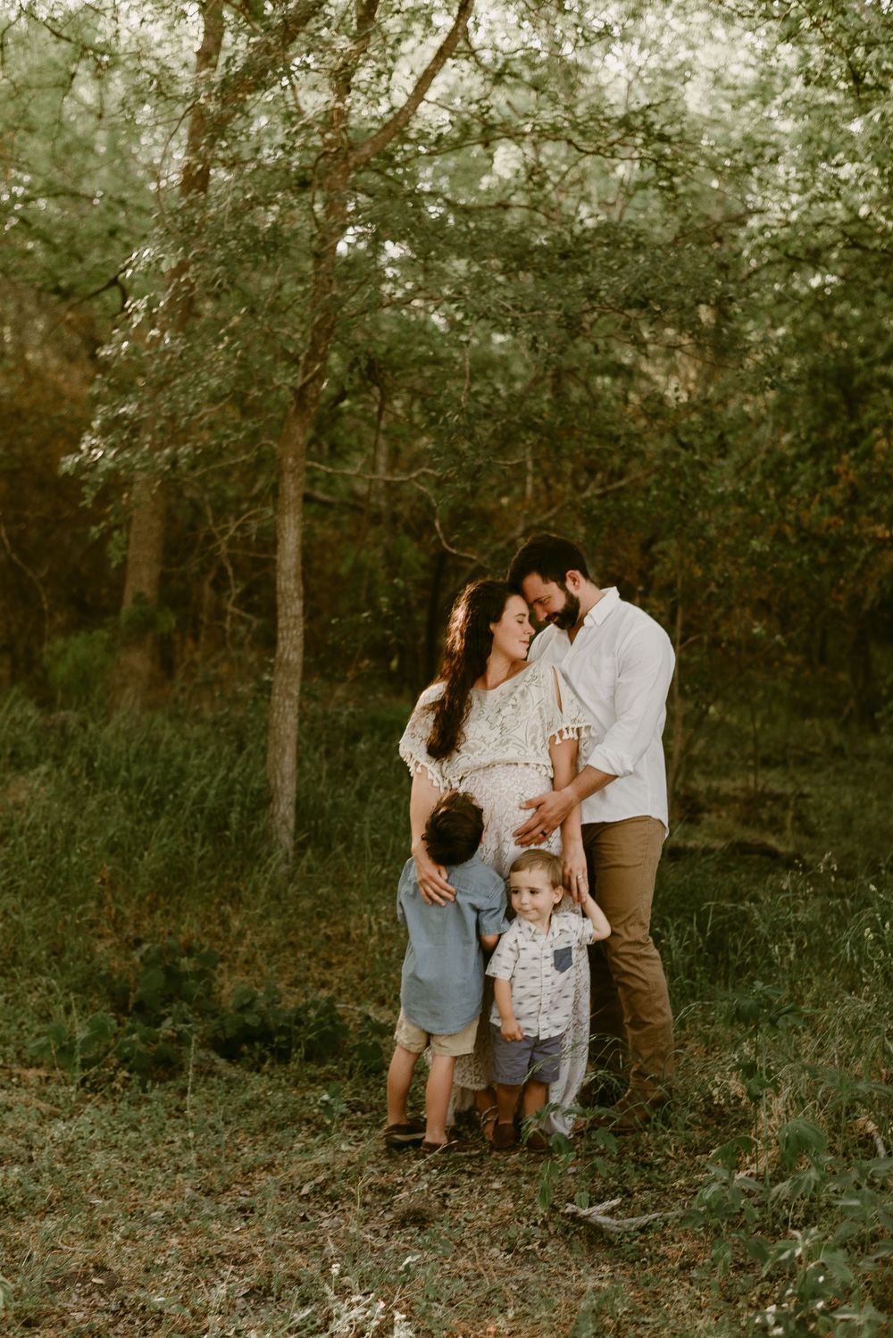 A family gathers close together in a dreamy forest setting during golden hour.