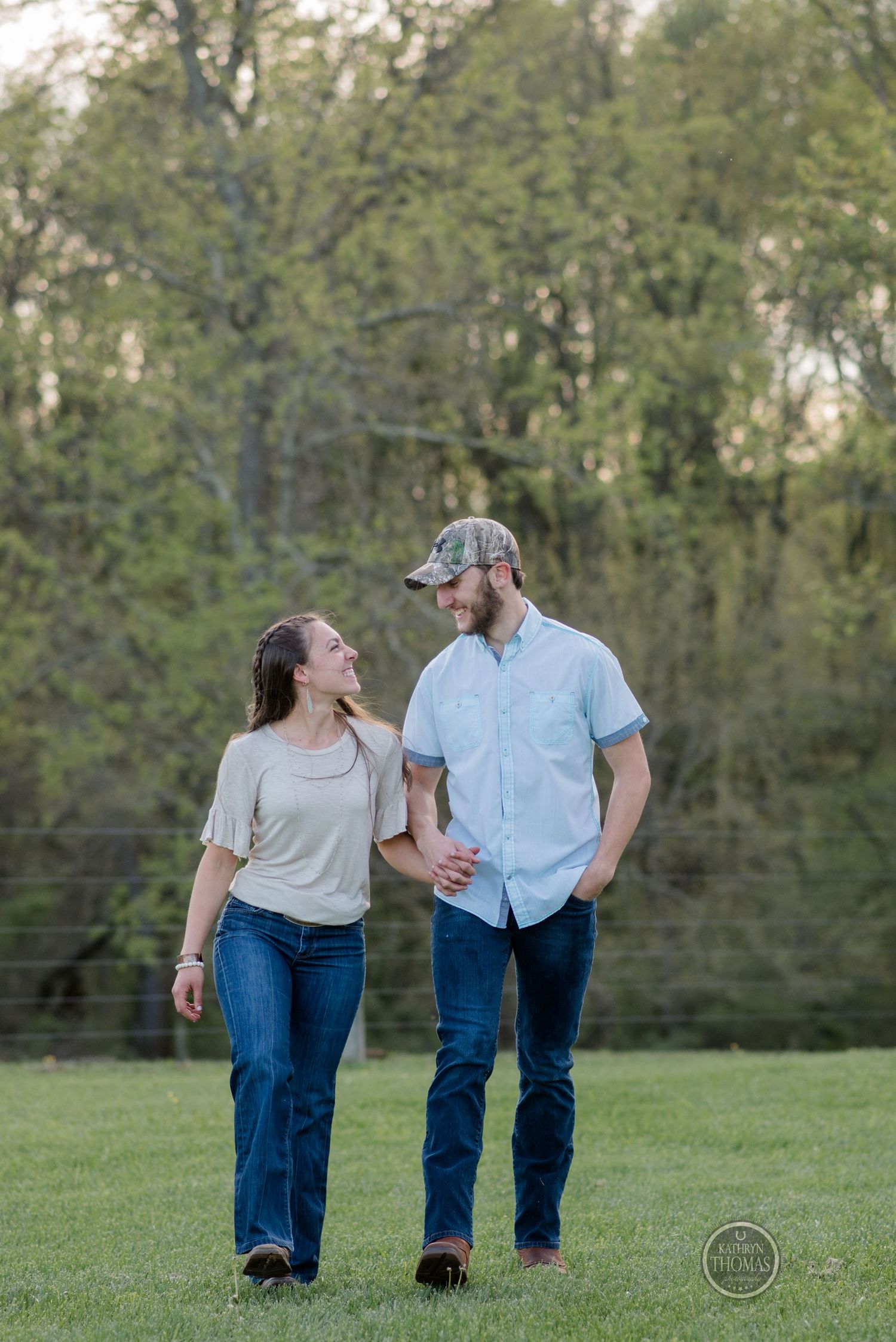 A couple walks together and shares a laugh in a grassy field at dusk.