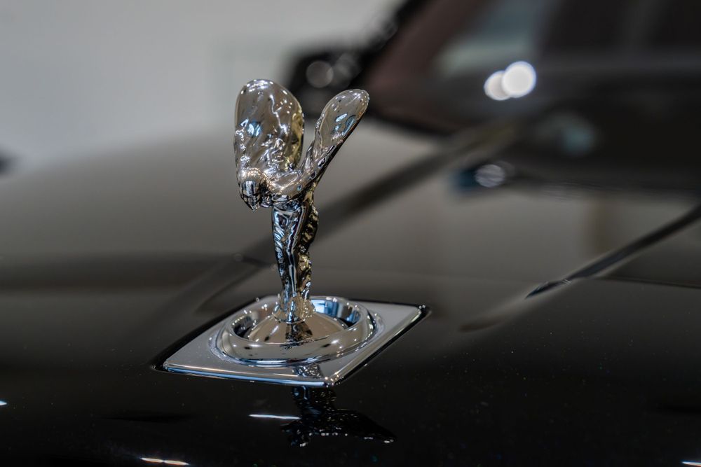 Close-up of the iconic Rolls-Royce Spirit of Ecstasy hood ornament on a black vehicle.