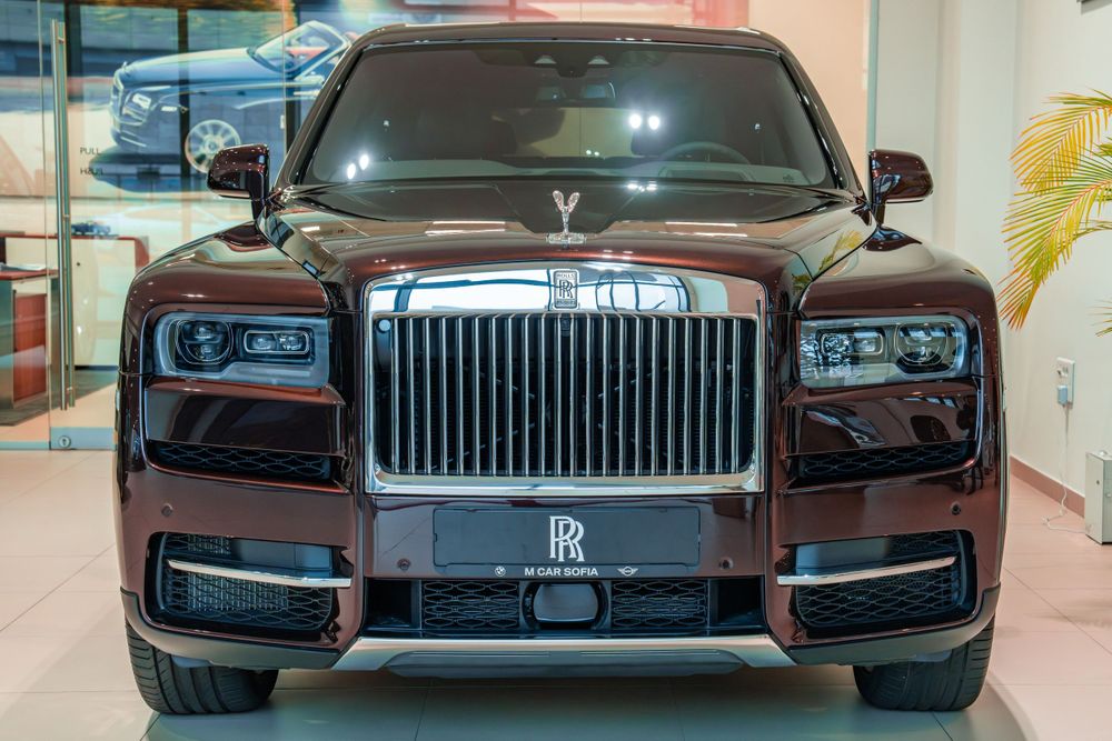 Front view of a maroon Rolls-Royce Cullinan showing its iconic chrome grille and LED headlights.