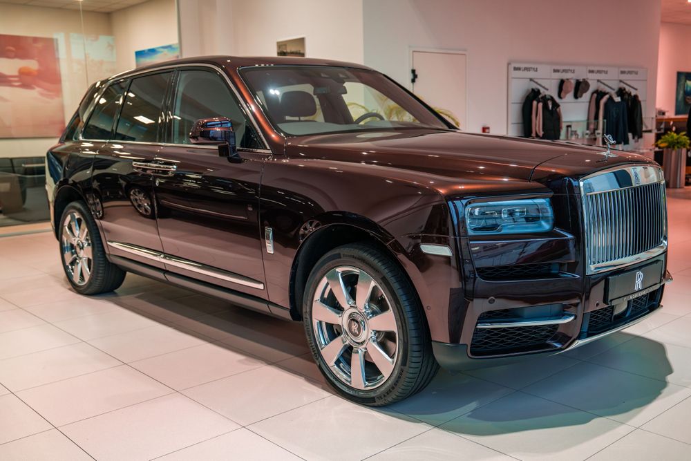 Side view of a burgundy Rolls-Royce Cullinan in a pristine showroom environment.