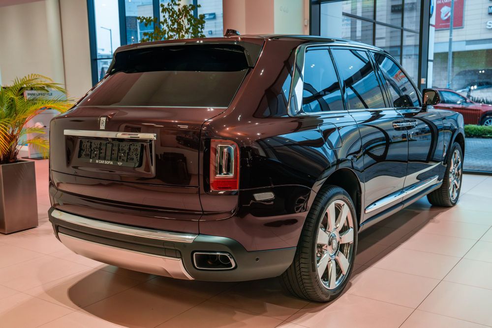 Rear three-quarter view of a dark burgundy Rolls-Royce Cullinan SUV in a dealership.