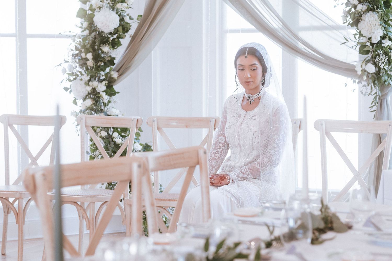 A bride sits near a window covered in natural light.