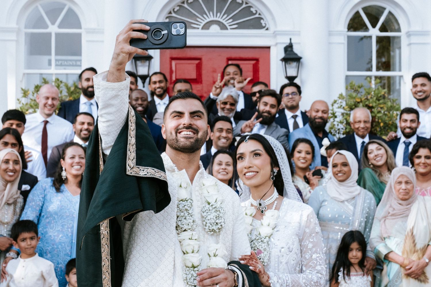 A groom takes a selfie of himself, his bride and their wedding guests.