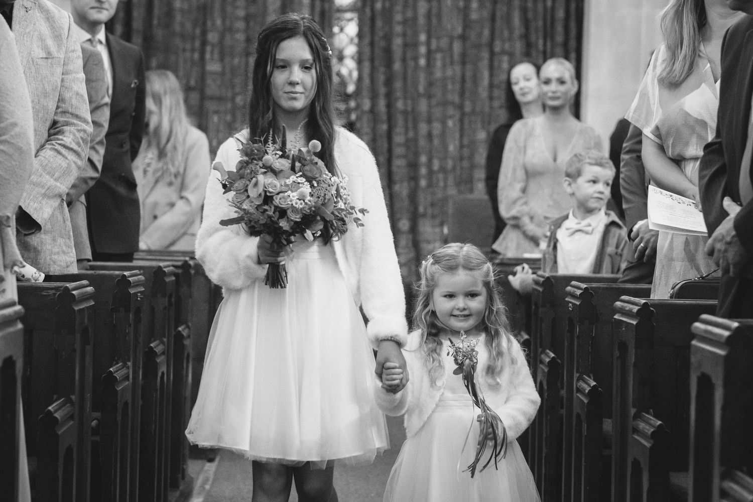 A bridesmaid and a flower girl walk down the aisle of a church wedding.