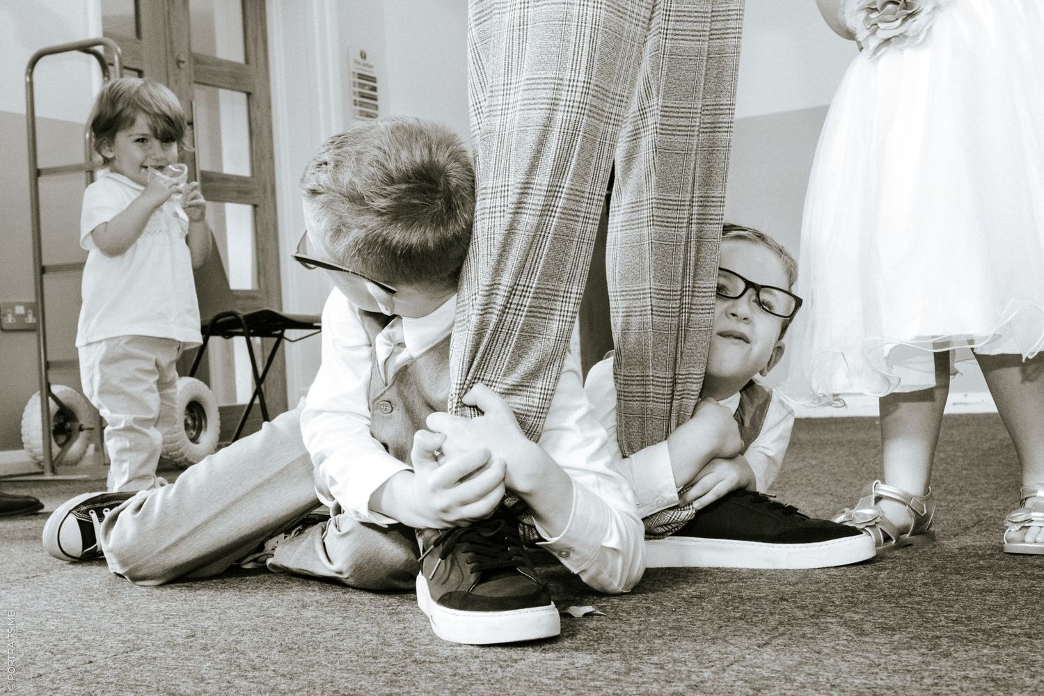 Two young boys with glasses hold on to a groom's legs at his wedding.