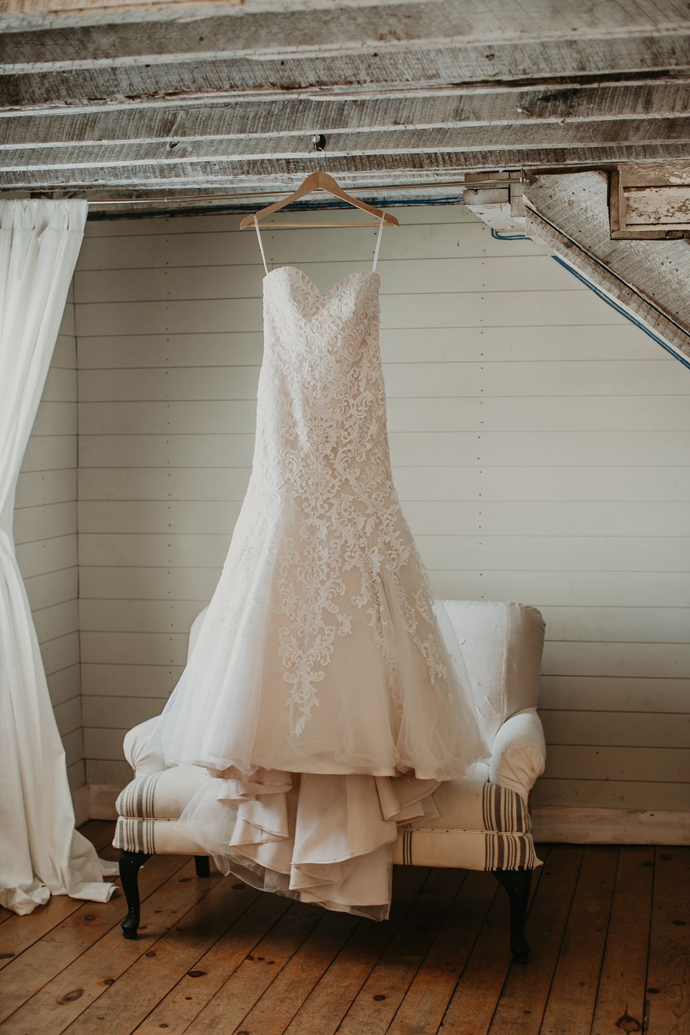 Elegant strapless lace mermaid wedding dress hanging on wooden hanger in rustic barn bridal suite.