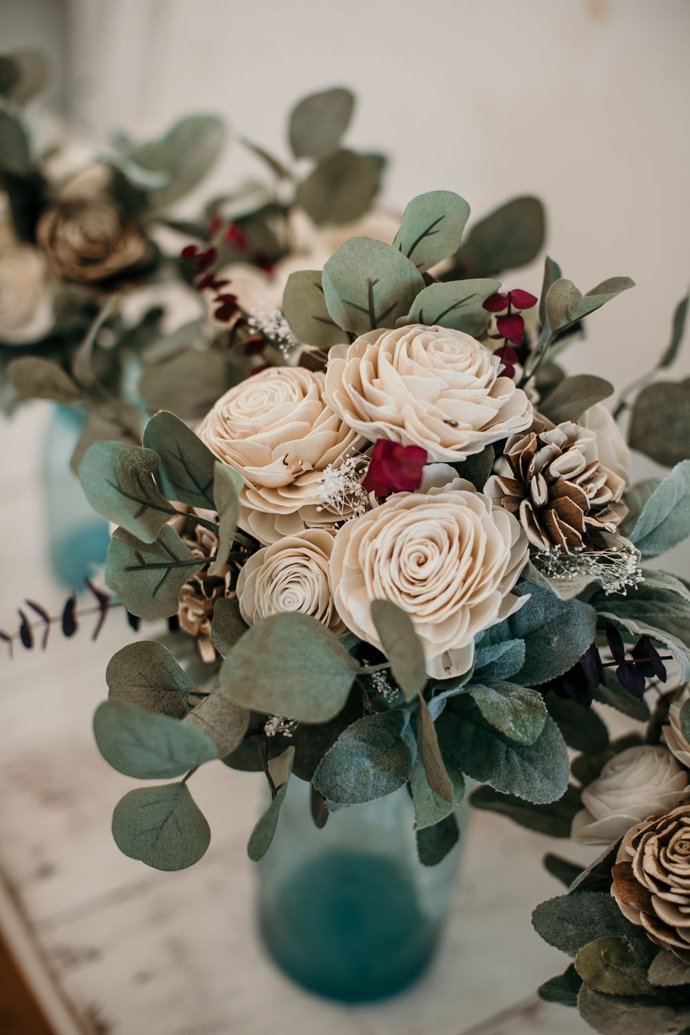 Elegant wedding bouquet with cream sola wood roses, burgundy accents, and eucalyptus in a teal vase.