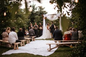 Outdoor wedding ceremony with wooden benches and string lights in a garden setting.