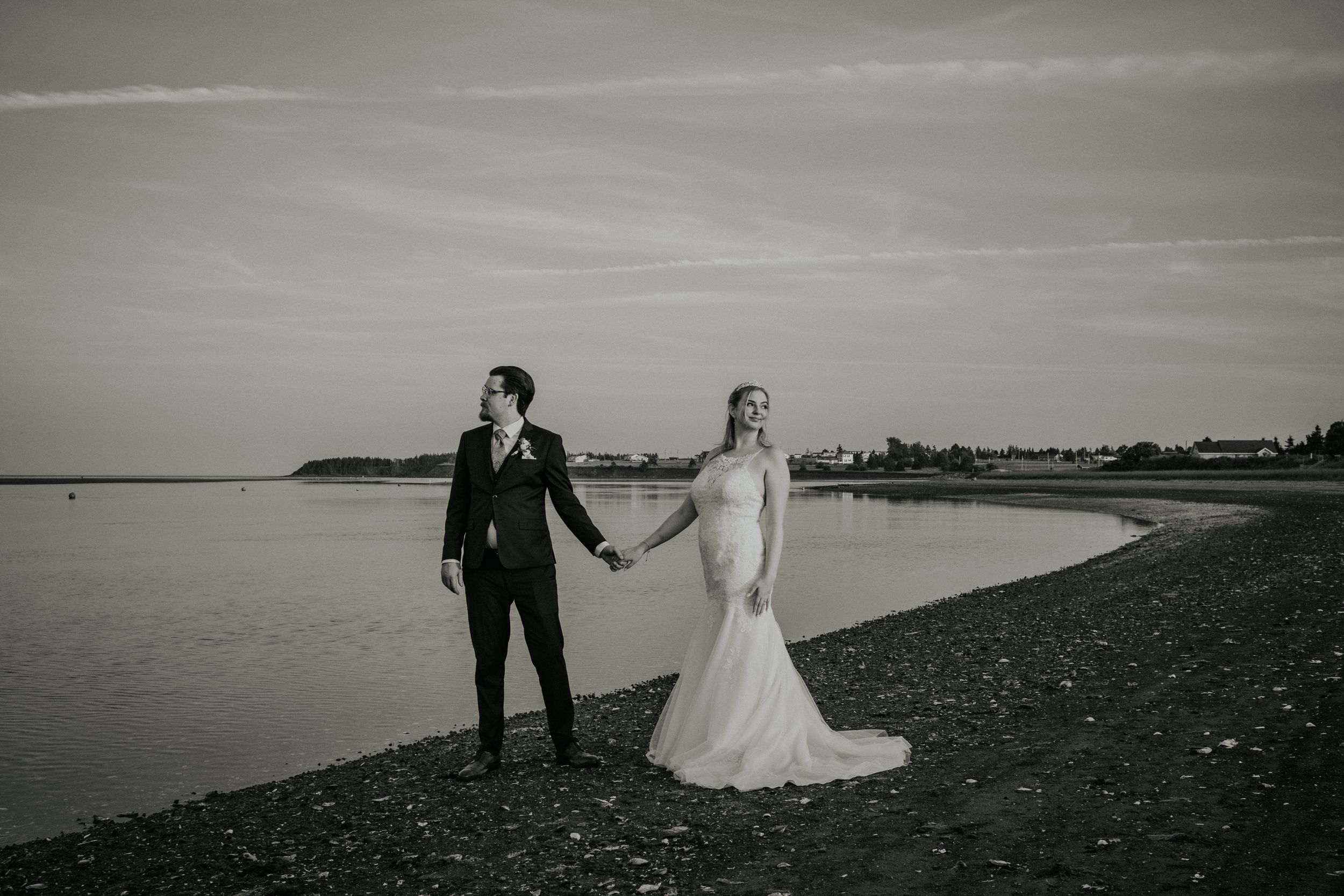 Black and white portrait of newlyweds holding hands on a beach shoreline. Photo at Fiddling Fisherman Lookout Souris PEI