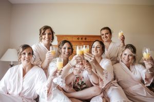 Bridesmaids in matching robes toast with champagne during wedding preparations. Photo at Rodd Crowbush