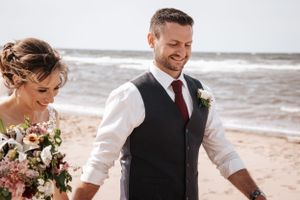Happy couple shares a moment together on a windy beach with beautiful bouquet. Photo at Rodd Crowbush
