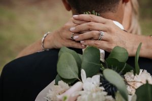 Close-up of hands with wedding ring holding bouquet with eucalyptus leaves.