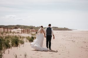 Couple walks hand in hand along a scenic beach with sand dunes. Photo at Rodd Crowbush