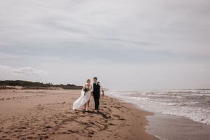 Newlyweds stroll along the shoreline as waves crash on the beach. Photo at Rodd Crowbush