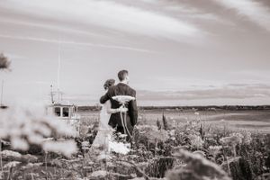 Black and white photo of couple embracing in a field with distant horizon.