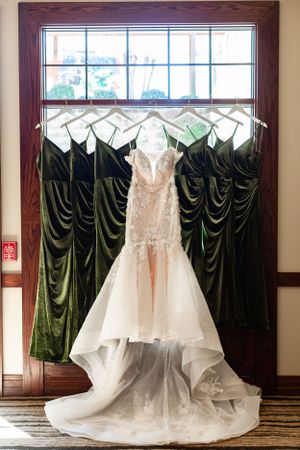 A white wedding dress and green bridesmaids' dresses hang in front of a window waiting to be put on for the wedding ceremony in Houston, TX.
