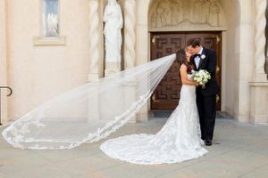 Bride's long veil flows in the wind behind her as she and her new husband share a kiss after their church ceremony in Houston, TX.