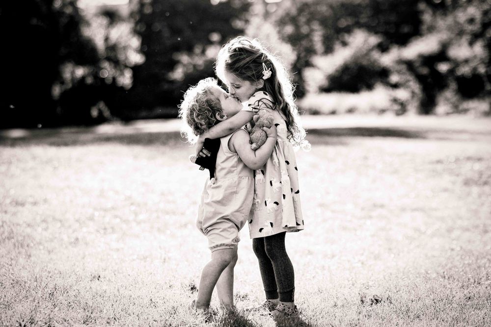 Two young sisters clutch onto soft toys and kiss each in a field on beautiful sunny day
