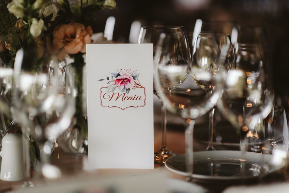 Wedding menu card with pink floral design alongside wine glasses on formal table setting.